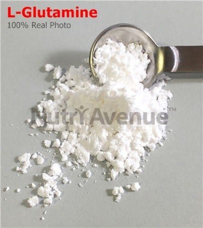 A close-up photograph of white, powdery L-Glutamine supplement piled on a gray surface with a metal measuring spoon scooping some up. The text "L-Glutamine" in red and a "NutriAvenue" watermark are visible.