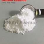 A pile of fine white powder, labeled "Instant Leucine," next to a metal measuring spoon filled with the powder.