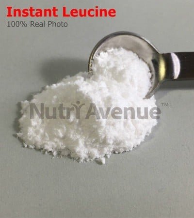 A pile of fine white powder, labeled "Instant Leucine," next to a metal measuring spoon filled with the powder.